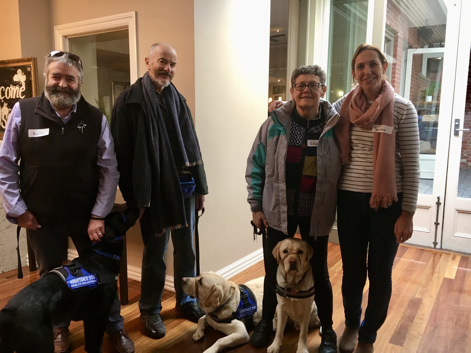 A group of Bigger Hearts community members gathered together at a Ballarat venue, smiling with their dementia assistance dogs.